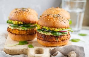 Healthy baked sweet potato burger with whole grain bun, guacamole, vegan mayonnaise and vegetables on a board. Vegetarian food concept, light background.